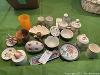 Full array of porcelain and ceramic items arranged on green tablecloth including dishes, containers, ring holder, soap dish, egg timer, and cups.