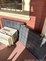 Panels of metal I Crate dog crates stacked on a porch, some showing wear and tied with yellow cords
