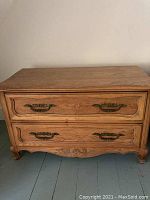 Front view of wooden dresser showing two drawers with ornate metal handles and carved details at the base and drawer fronts, surface shows wear and watermark.