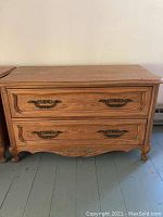 Front view of the wooden two drawer dresser showcasing carved designs, metal drawer handles, and curved bottom detailing.