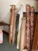 Six assorted bolts of fabric standing upright showing a range of solid colors and floral patterns.