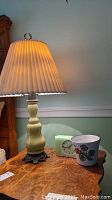 Glass base table lamp with pleated shade, green Big Ben Moon Beam clock, and flower decorated cache pot on wood table