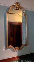 Wall-mounted tall rectangular mirror with arched top and ornate antique gold color frame showing signs of wear and age.