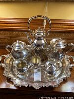 Full tea and coffee set arranged on ornate rectangular silver plated tray with warming stand under teapot.
