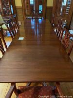 Top view of large antique dining table fully extended with chairs around, wood is dark polished with minor surface scratches visible.