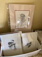 Original pencil drawings in frames showing cat themes, wrapped in plastic for protection