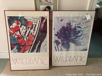 Two framed prints titled Wildbank, one with red flowers and one with purple flowers, both featuring newspaper background and red text at bottom.