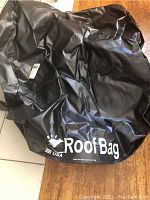Photo of black car roof bag with 'Roof Bag USA' logo printed on it, laid flat showing size and material.