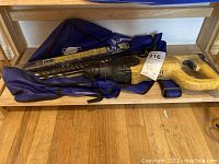 Rotary hammer and bits laying on blue carrying bag on a wooden shelf.