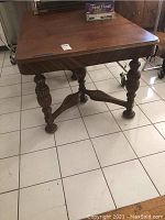 Full view of the vintage square dining table made of dark wood showing the top and legs.