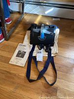 Dremel router/shaper table with blue knob adjustment arm and straps on wooden floor, including Dremel manual beside it.