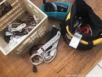 Multiple electrical cords, surge protectors, and a black fabric tool bag filled with red, black, and white cables on the floor plus a small blue basket containing device chargers and connectors.