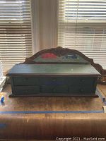 Front view of green wooden jewelry cabinet with six drawers, showing carved floral decorative top panel and slight wood surface wear.