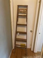 Front view of the wooden ladder showing all six steps and overall height against a wall.