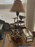 Full view of fountain lamp with leaf and dolphin motifs showing round marble stone base, jewelry box and railroad spike on table