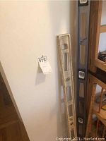 Photo showing a worn 6-foot aluminum Empire level with magnetic strip and bubble vials leaning against the wall.