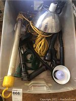 Plastic bin containing long fluorescent tube light fixture, metallic dome lamp shade, yellow extension cord, several flashlights, floor lamp, and desk lamp all mixed together