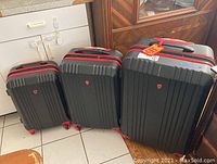 Three hard shell black suitcases with red accents, upright on tiled floor, varying sizes including two small.