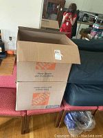 Two sealed cardboard boxes from Home Depot stacked on a patterned cloth surface.
