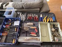 Top-down view of assorted hand tools spread on a table including screwdrivers, wrenches, masonry trowels, wire cutters, and others.