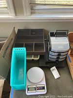 Multiple plastic storage bins including a light blue vertical bin, a gray multi-compartment organizer tray, a black and metal clipboard with calculator and storage compartment, and a white SF-400 kitchen scale.