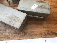 Two gray metal tool boxes with signs of wear and one labeled with handwritten tags.