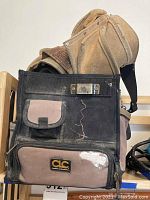Photo showing the black and gray CLC electrician's tool bag with visible wear and tear, small front flap pocket, and metal hardware at top.