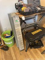 Full view of the workbench with saw horses, bucket of tools, toolbox and charger underneath