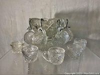Full punched bowl set with six small matching cups arranged around it, showing detailed cut glass pattern.