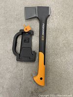 Fiskars X11 cutting tool standing upright next to its black safety holster with orange lock.