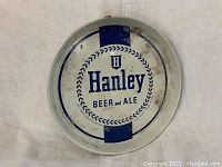Front side of the vintage Hanley Beer metal tray showing logo and wear including rust and discoloration.