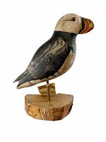 Side profile of puffin decoy mounted on a rustic wooden base showing detailed carving and paintwork on light background.