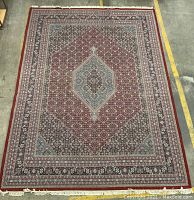 Full view of rug laid on warehouse floor showing overall pattern and fringe.