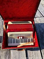 Accordion open in red velvet-lined case showing piano keyboard and strap