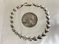 Top view of the vintage sterling silver heart link bracelet laid out flat with a 1961 quarter for size comparison.