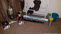 Overview photo including Shark vacuums, white metal extendable shoe rack with shoes and boots, wooden and metal wall mount hook racks, reusable cups and large plastic jug for drinks.