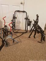Photo showing the three different sports racks arranged on a carpeted floor against a white door, showing the steel adjustable rack with red hooks and two black bicycle racks with padded sections.