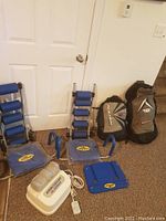 Two Ab Rocket abdominal exercise machines with blue padding and sturdy bases, Evergain electric leg stimulator device with wired remote, two Naish kite surfing sails in bags