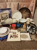 Photo shows full collection of items including white frying pan, black and white Teflon kettle, slow cooker with locking lid, zodiac Pyrex dish, porcelain mugs and plates, multiple frames, ribbons, gloves, wax bear and others.