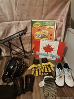 Photo of boys sports items, Crayola Minions coloring book, and Canada-Opoly board game showing bike rack, helmet, gloves, shin guards, knee braces, soccer shoes, and board games.