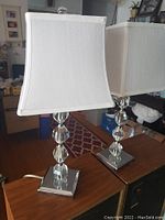 Pair of crystal table lamps with faceted crystal bases and white fabric shades on square metallic bases.