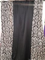 Two black and white patterned curtain panels with one black blackout curtain panel hung.