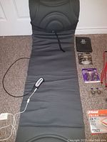 Full view of Dr. Scholl's seat massager with remote control, and other lot items including Obus Forme seat massager, packaged headlights, car manual cover, and other small accessories laid on floor.