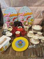 Full lot photo showing teapots, mugs, plates, Easter decorations and utensils arranged on table