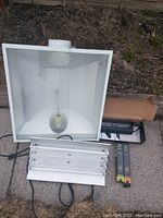 Overview image of grow light fixture and components on outdoor ground, shows reflector, ballast, and bulbs in packaging.