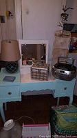 Antique teal vanity desk with fold-out mirror, lamp, CD/radio player, wooden toolbox, and other accessories.