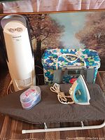 Photo showing all items including the ironing board, iron, humidifier, cooler bag, sewing kit, glass scale, and framed picture in the background.