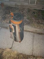 Full side view of the Mizuno golf club case standing upright outdoors on pavement showing black body with tan leather trim, multiple external zippered pockets and attached carrying strap.