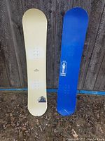 Photo of two snowboards - white One Fourty Two Circus and blue Liquid Man 1500, leaned against wooden wall