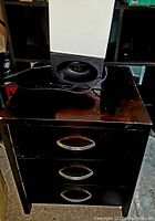 Small dark brown wooden dresser with three drawers and metallic handles.